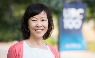 Photo of Phyllis Poon smiling in front of a UBC 100 flag